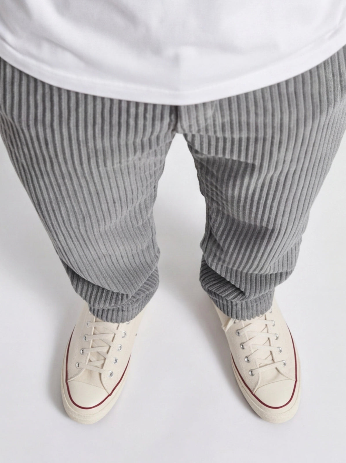 Gray striped pants and white sneakers on a light gray background