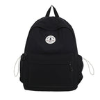 A black nylon backpack with a top handle, a front zippered pocket, side mesh pockets with drawstring cords, and a circular white logo patch on the front.