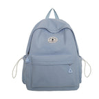 A light blue gingham backpack with a front zippered pocket, side pockets, and a circular 'The Minimalist' brand patch on the front, shown against a plain white background.