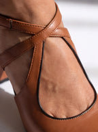 Close-up of a brown leather shoe with criss-cross straps.